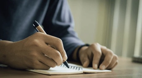 Person notiert handschriftlich Stichpunkte in einem Notizblock am Schreibtisch